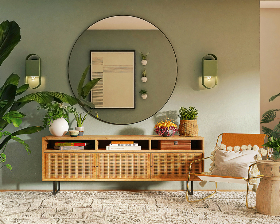 Ein Sideboard aus Holz und Rattan vor einer salbeigrünen Wand mit großem rundem Spiegel.