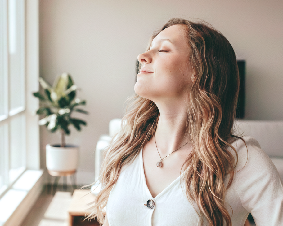 Eine Frau atmet mit geschlossenen Augen tief ein in einem Wohnzimmer.