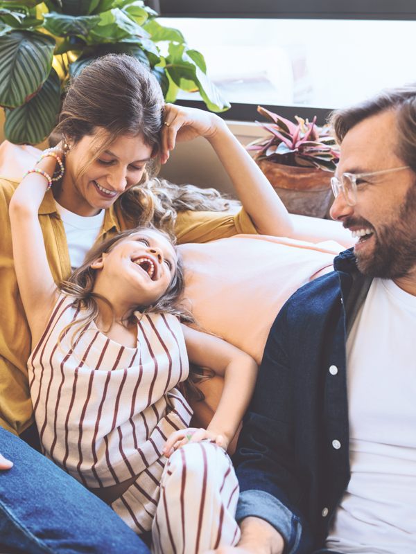 Eine Frau und ein Mann sitzen lachend mit einem kleinen Mädchen auf einem Sofa.