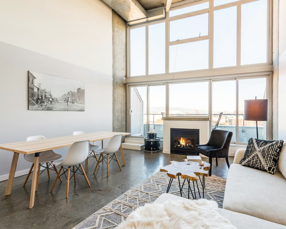 Loftwohnung mit weißen Wänden, großer Fensterfront und hellen Holzmöbeln.