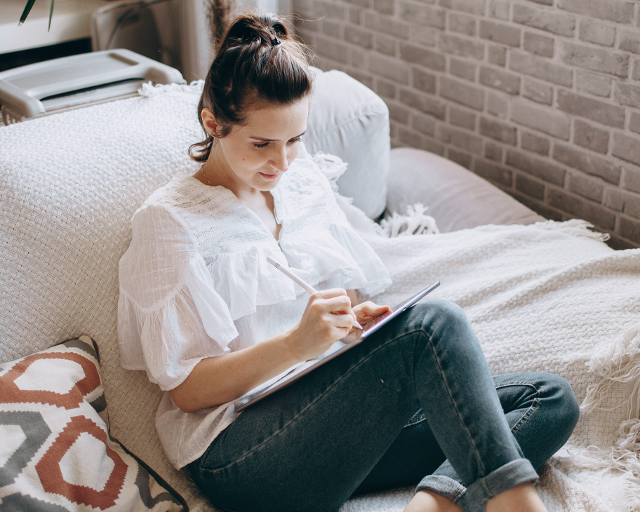 Eine Frau sitzt auf einem Sofa und zeichnet auf einem Tablet.