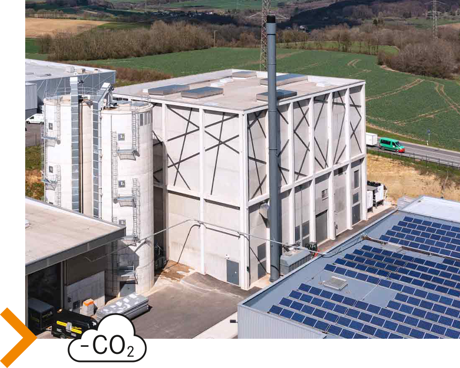 Ein Foto eines Holzheizkraftwerks und einer Photovoltaikanlage, davor ein Wolken-Icon mit der Aufschrift „–CO2“