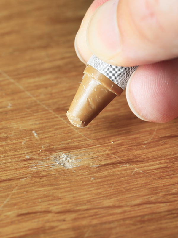 Hand mit Wachsstift bessert eine beschädigte Holzoberfläche aus.